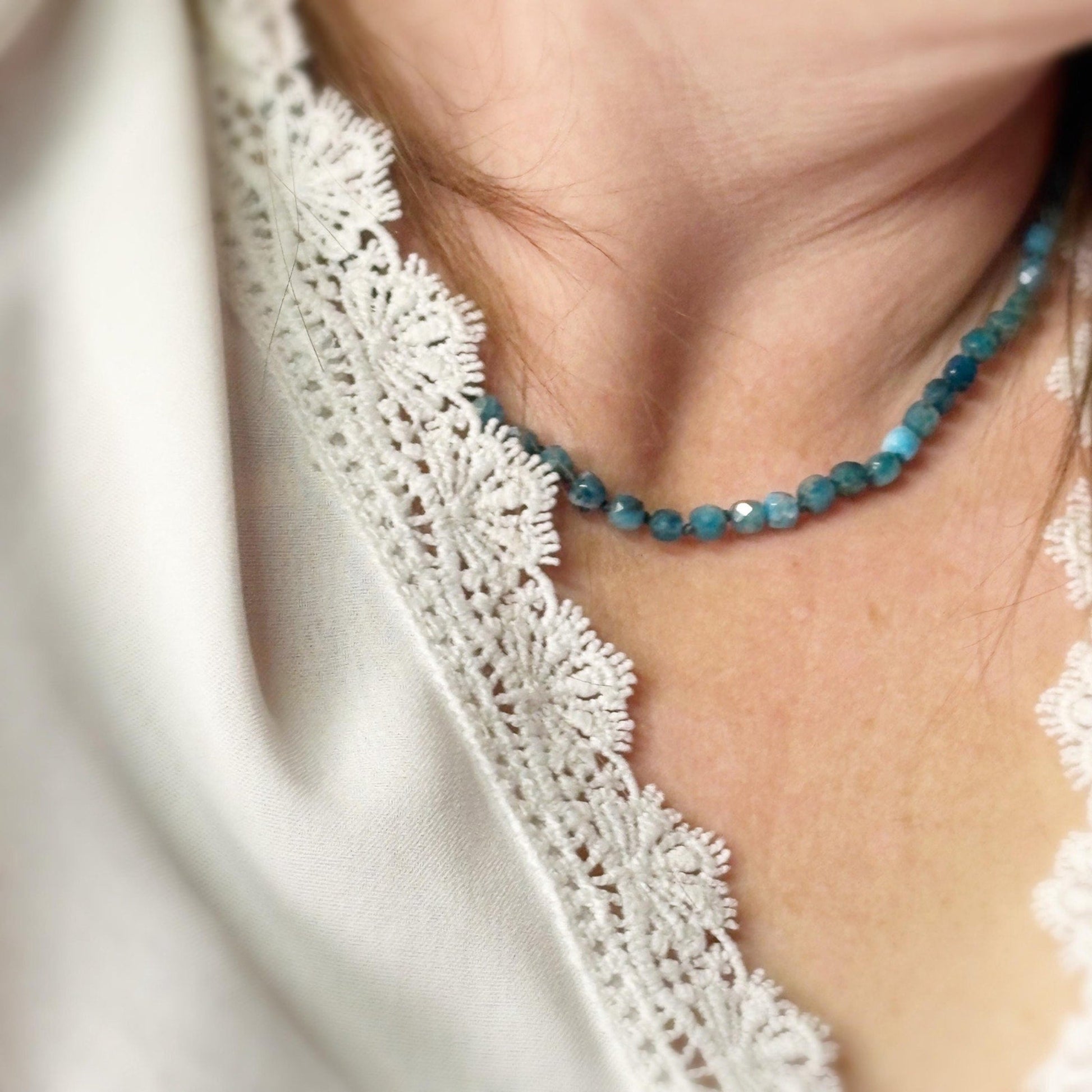Close-up of a person wearing a blue beaded necklace with a white lace garment.