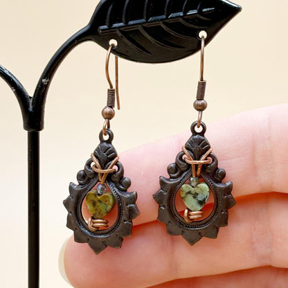 Pair of earrings with green gemstones held against a neutral background