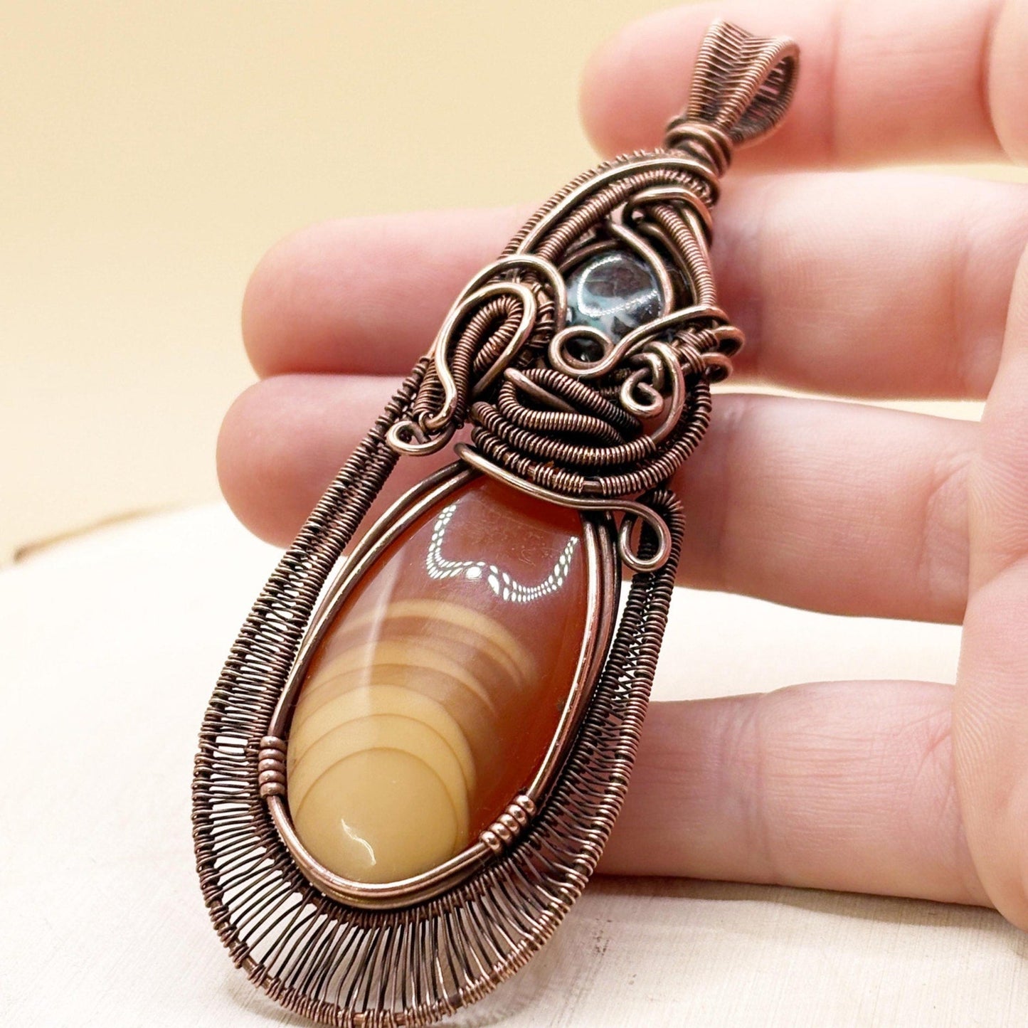 Hand holding a decorative pendant with 2 stones and intricate copper wirework.