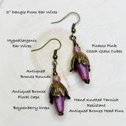 Pink glass cube earrings with bronze accents on a white background, featuring text details.