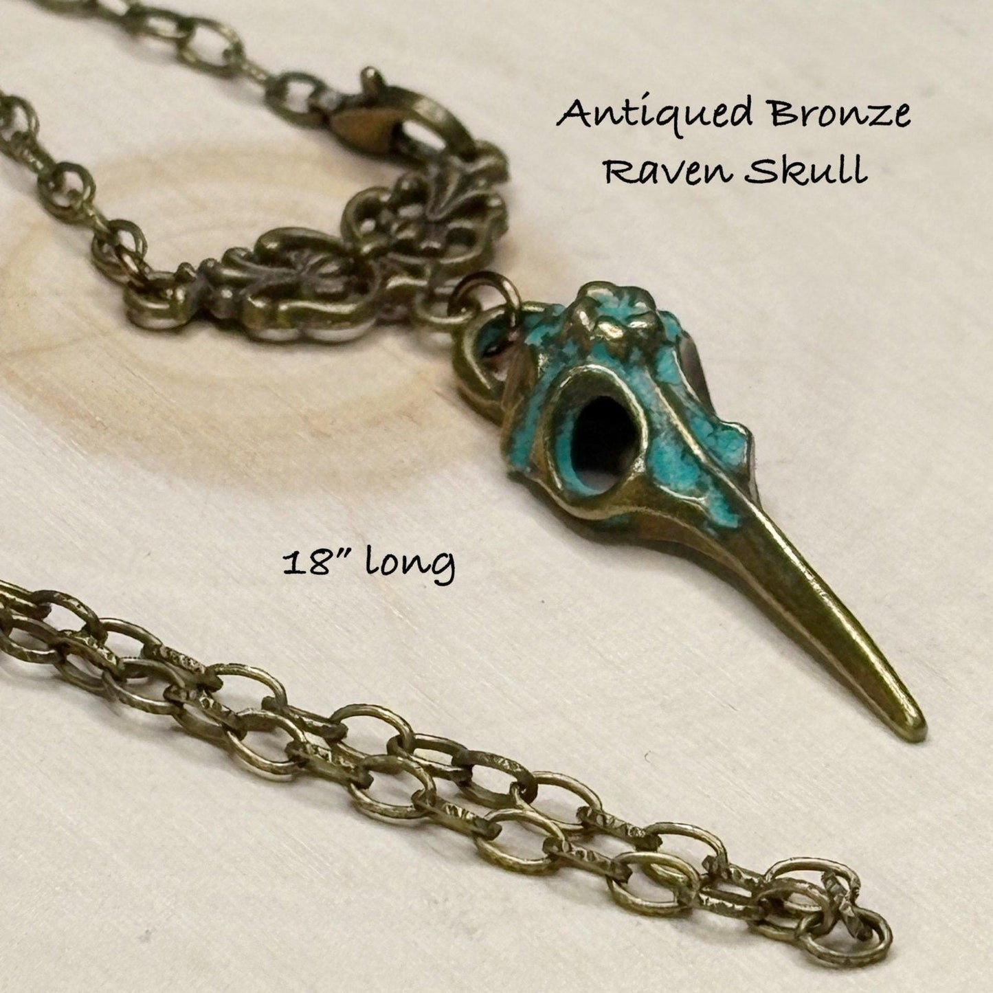 Antiqued bronze raven skull necklace on a light background