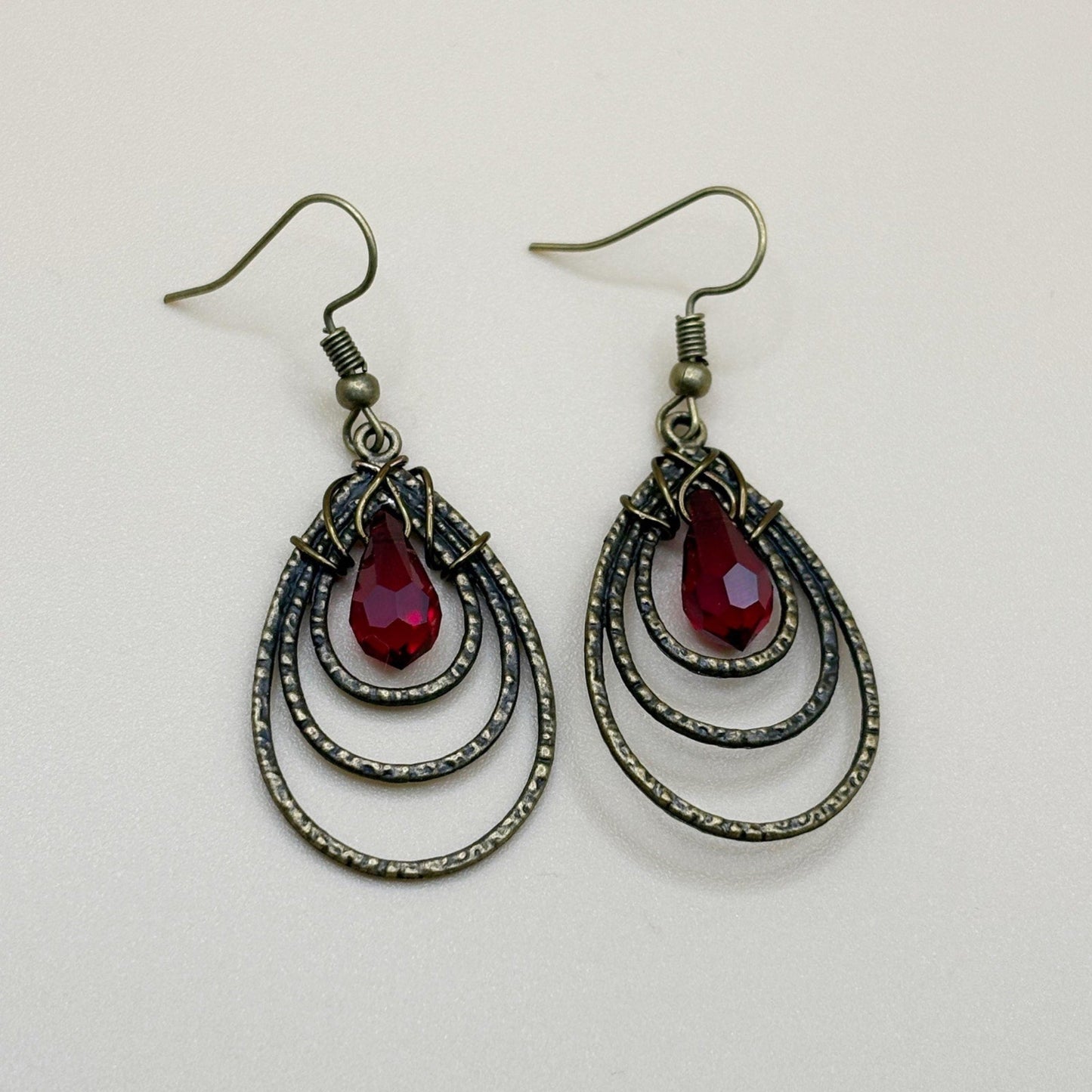 Pair of earrings with red teardrop stones and bronze teardrop focal designs on a light gray background