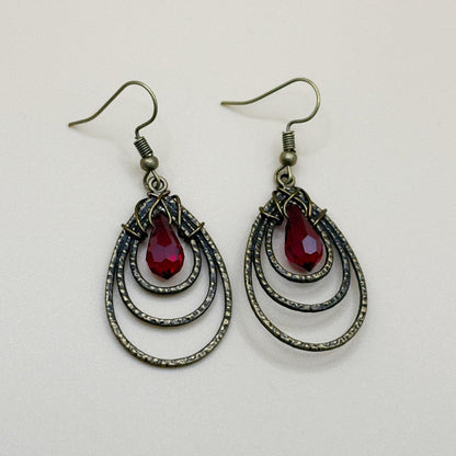 Pair of earrings with red teardrop stones and bronze teardrop focal designs on a light gray background