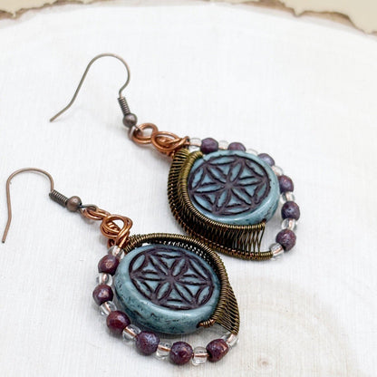 Pair of earrings with blue circular designs and purple beads on a white background
