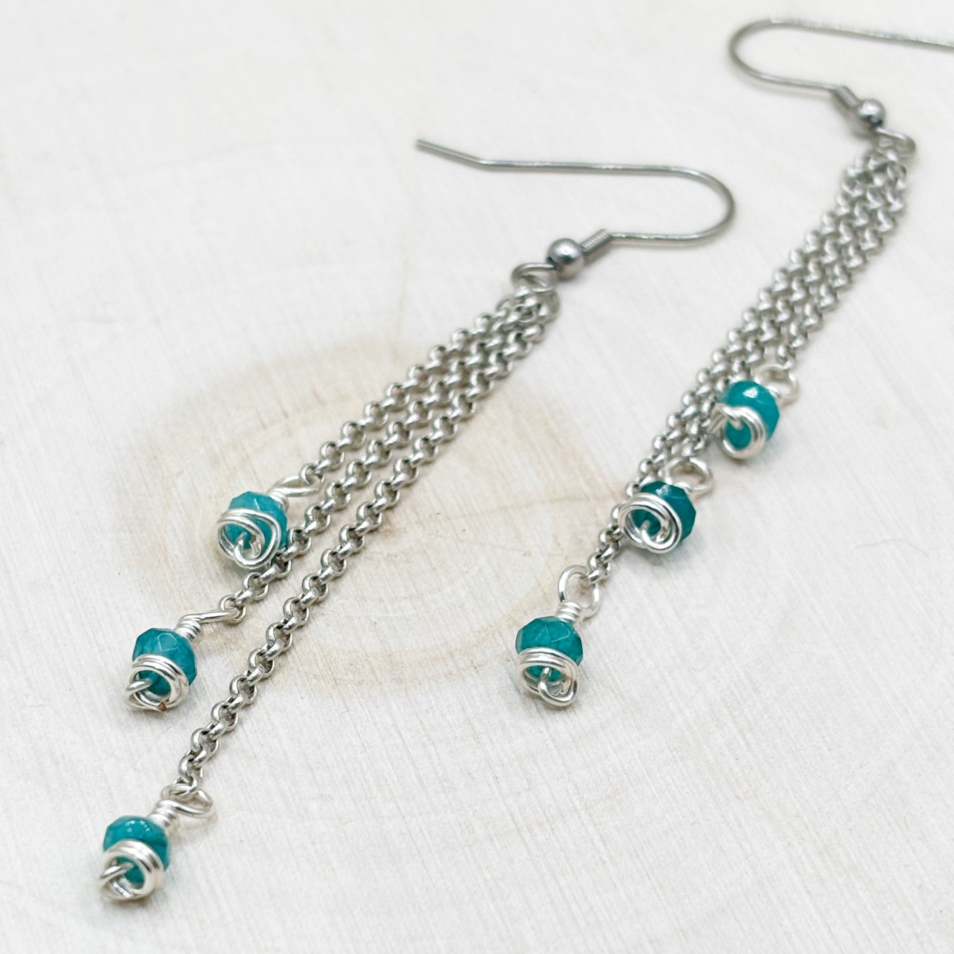 Silver chain earrings with blue agate beads on a white background