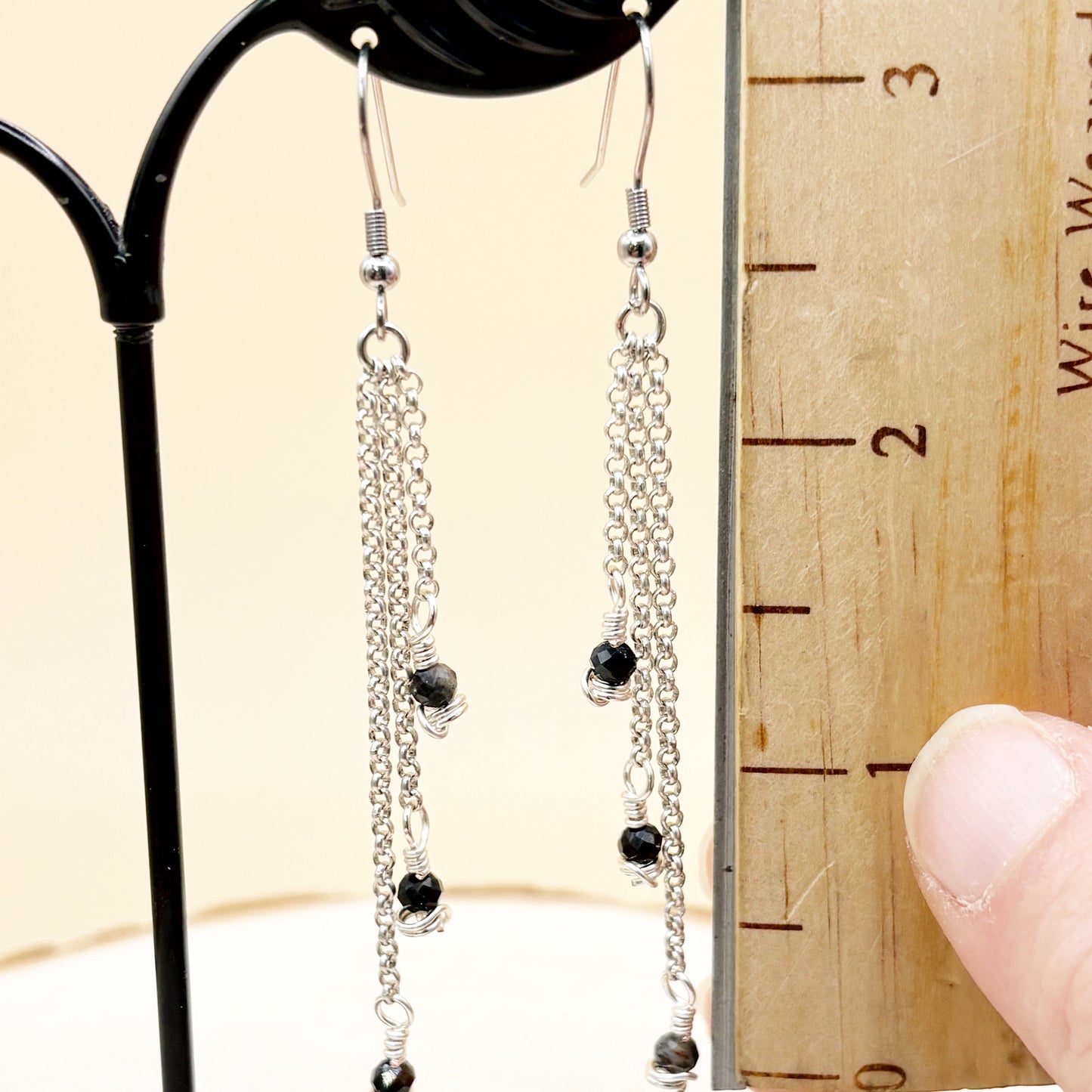 Silver chain earrings with blue beads on a wooden ruler for scale.