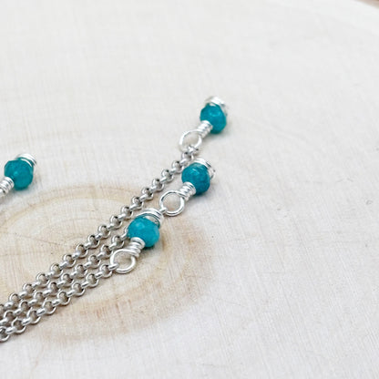 Silver chain necklace with turquoise beads on a light wooden surface