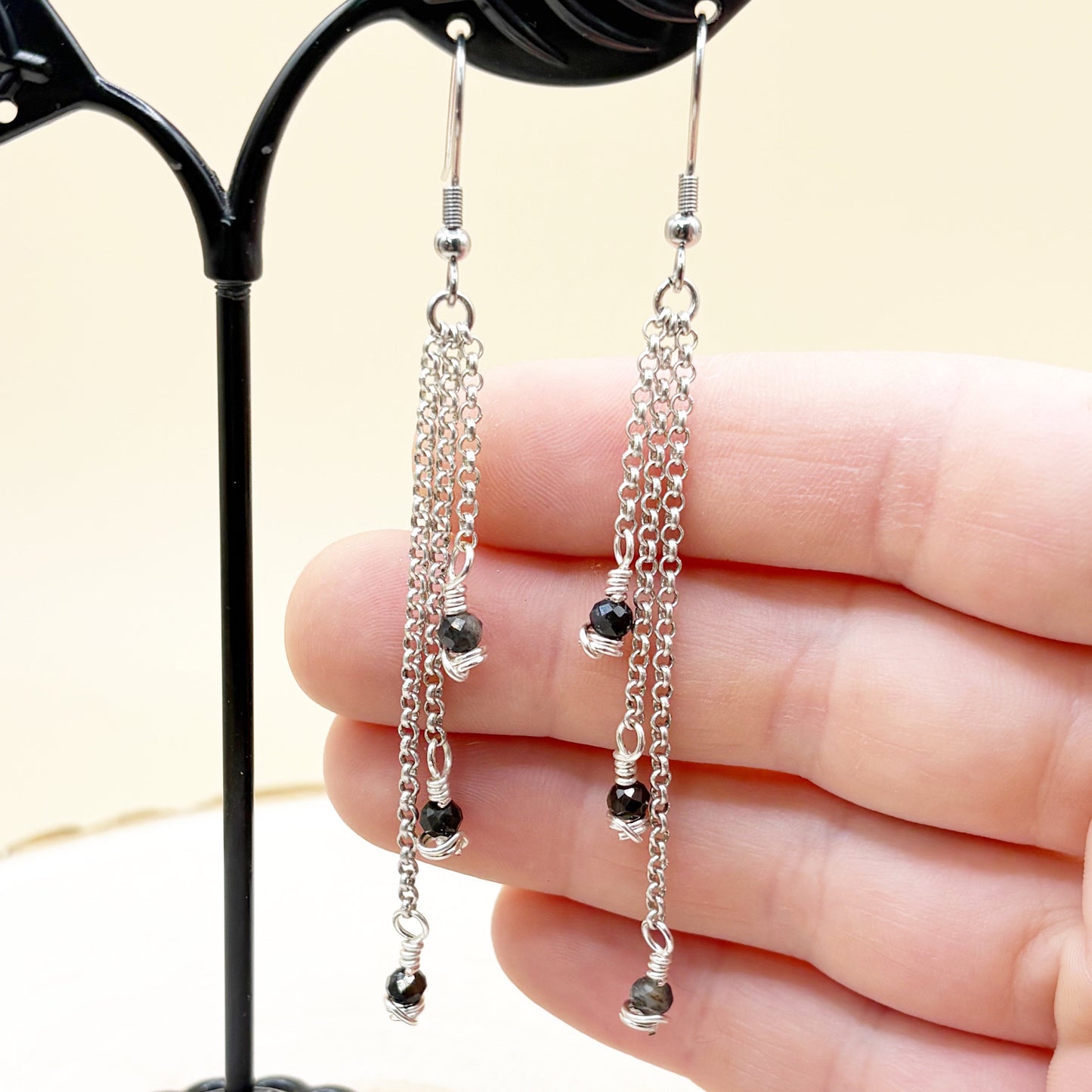 Silver chain earrings with blue beads held by a hand against a neutral background