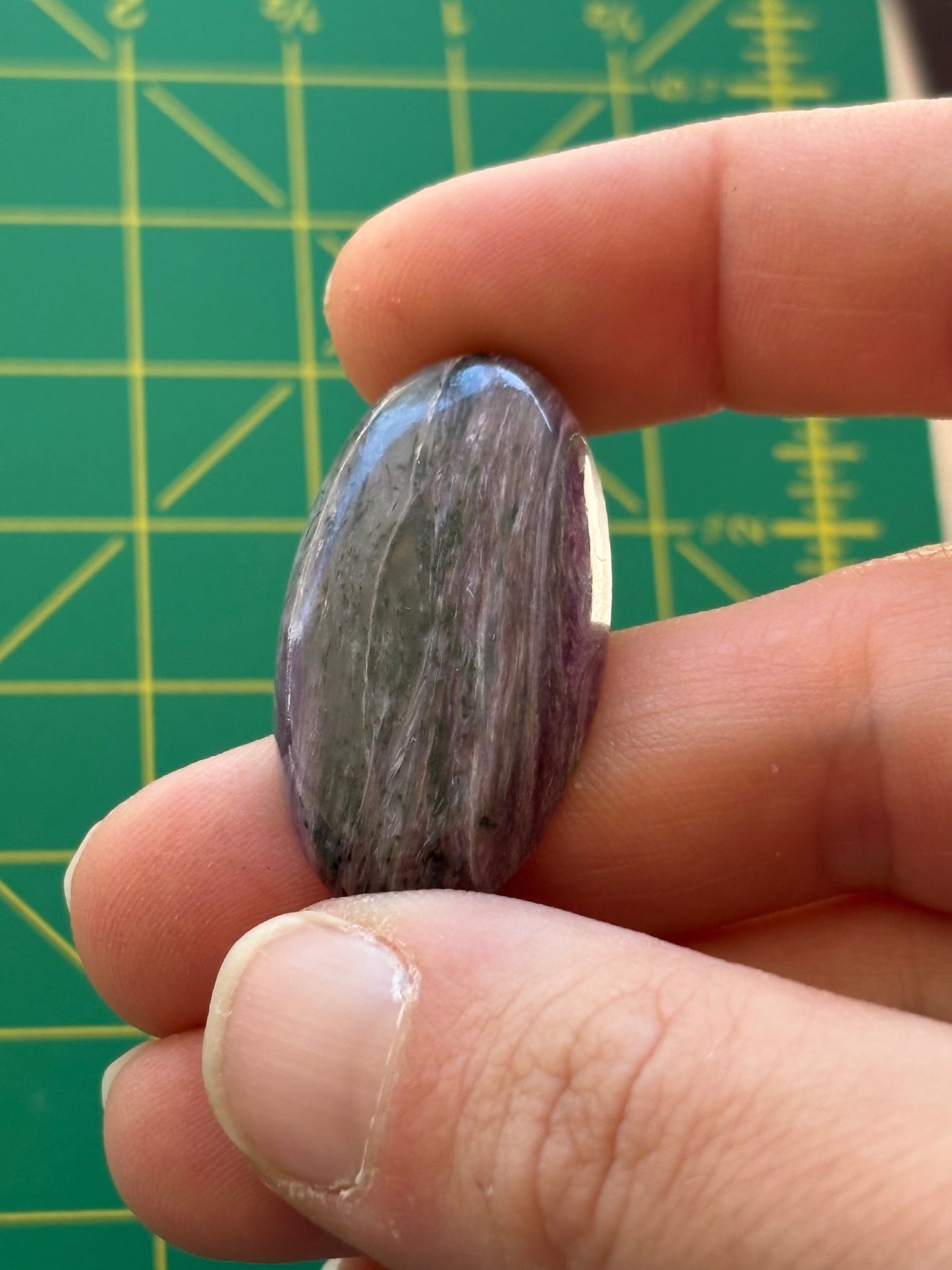 Hand holding a purple stone against a green cutting mat with grid lines