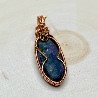 purple charoite stone pendant with copper wire wrapping on a light background showing back side