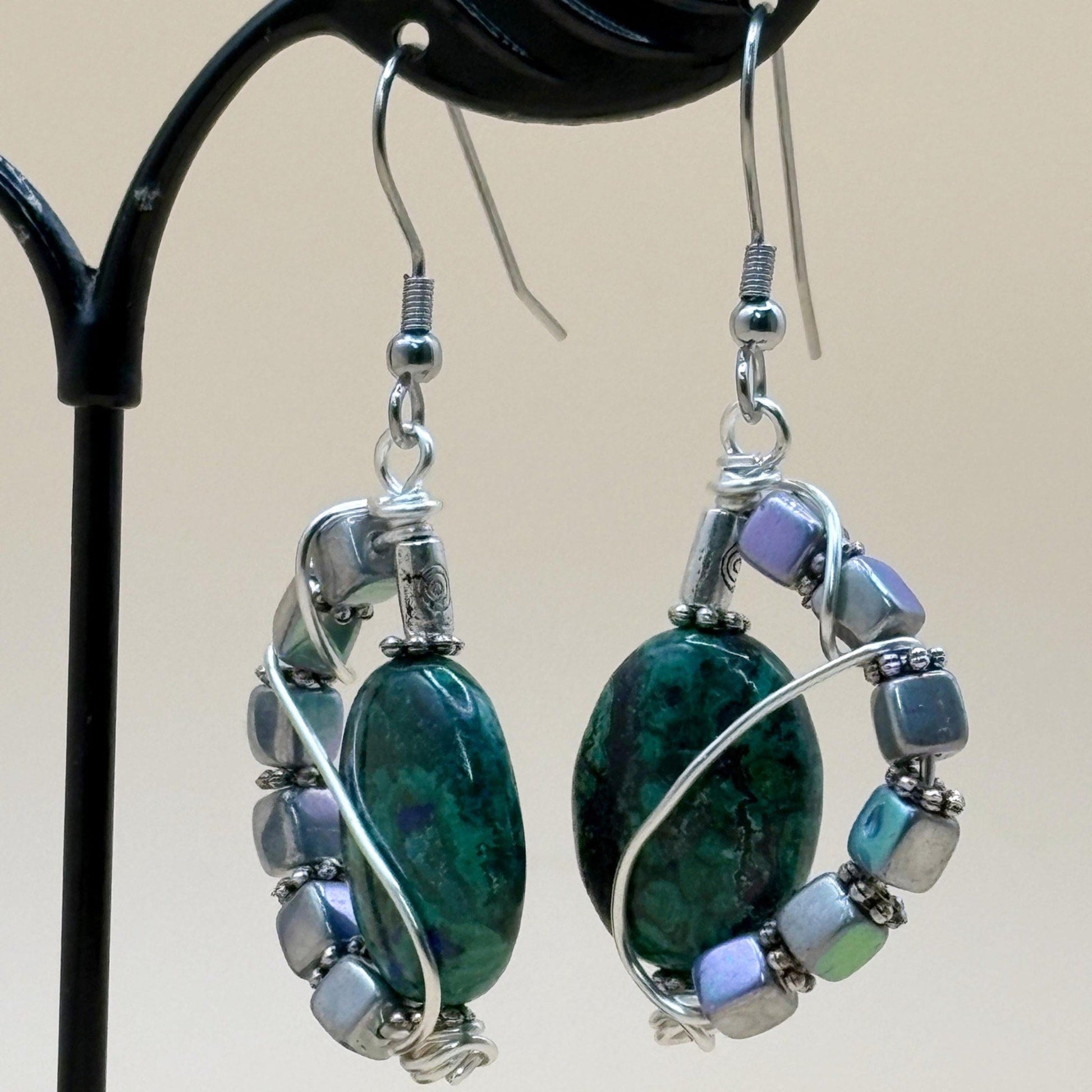 Pair of earrings with green stones and silver accents on a beige background