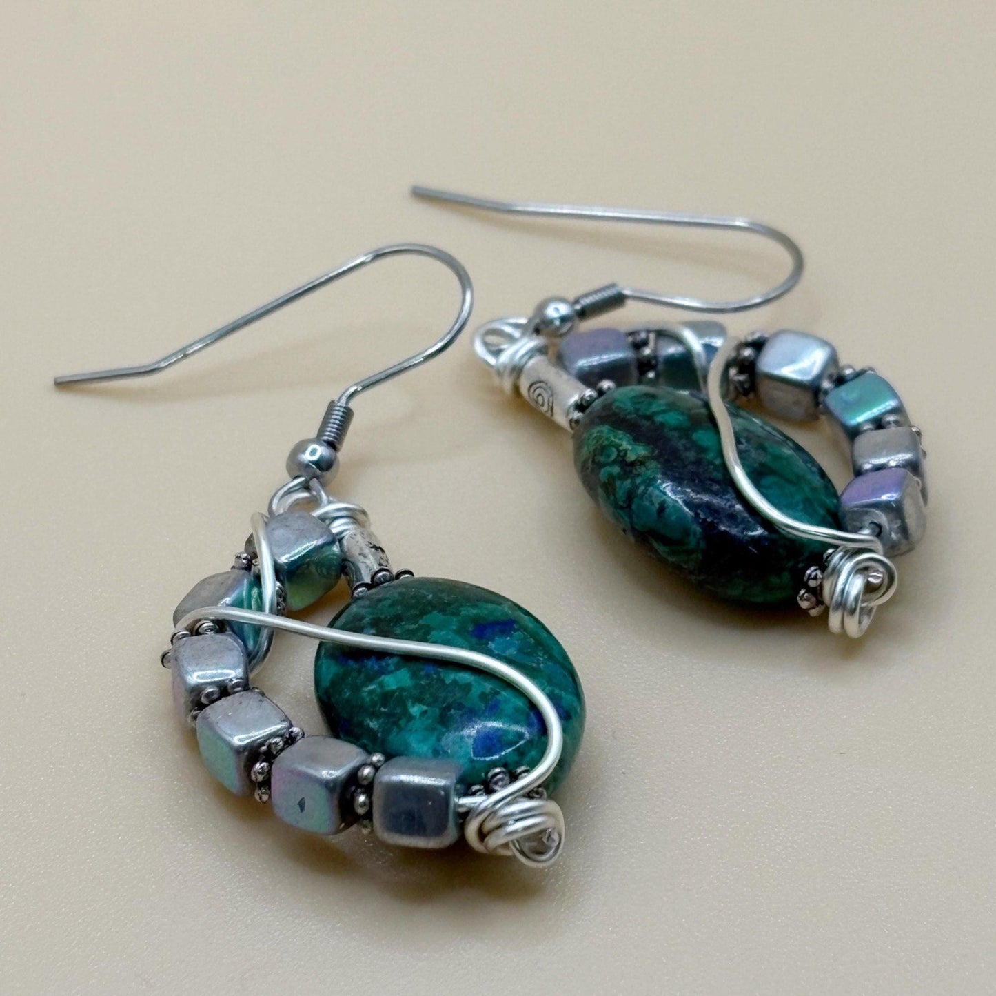 Pair of silver and green beaded earrings on a beige background