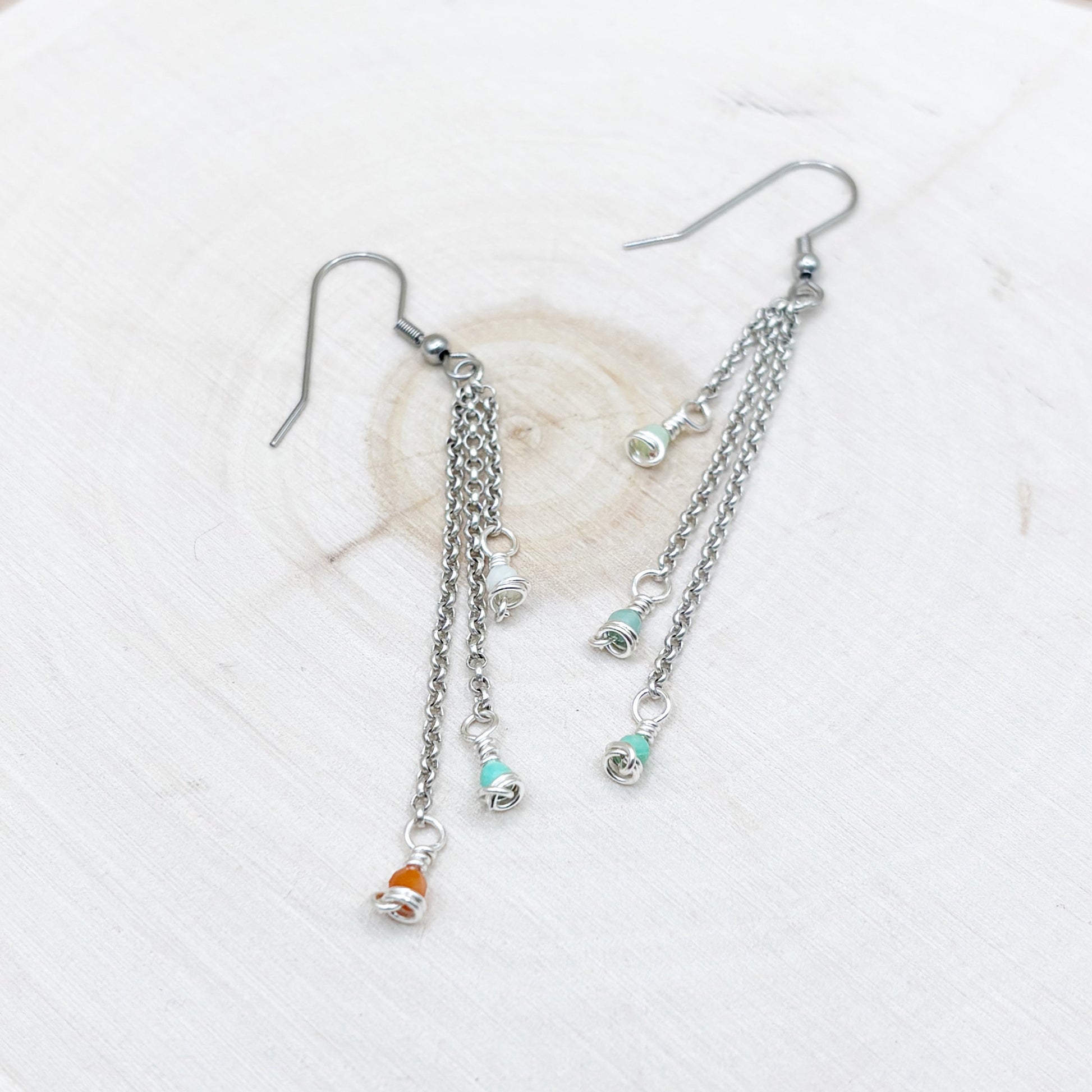 Silver chain earrings with small charms on a wood background