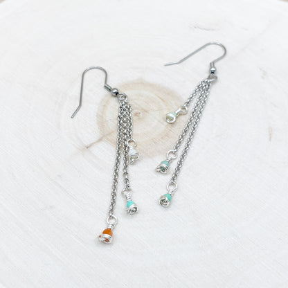 Silver chain earrings with small charms on a wood background