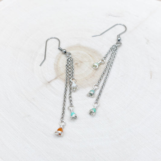 Silver chain earrings with small charms on a wood background