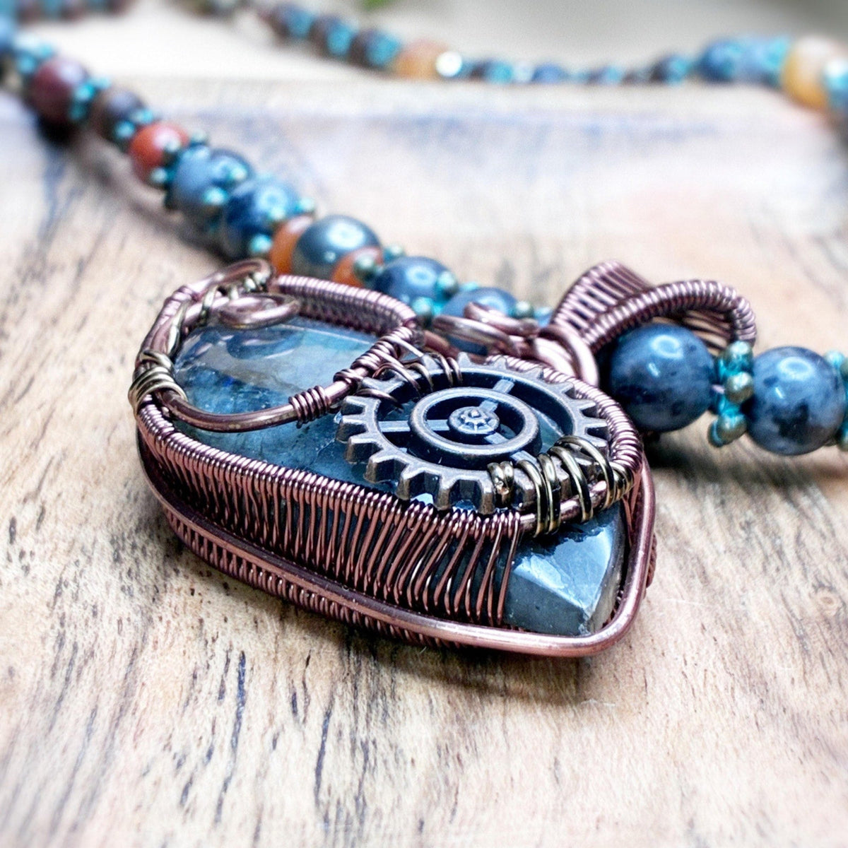 Handmade wire wrap in copper with a copper gear embellishment on a wooden background