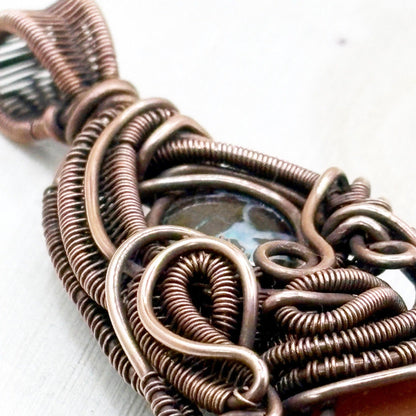 Close-up of a copper wire-wrapped pendant on a white background