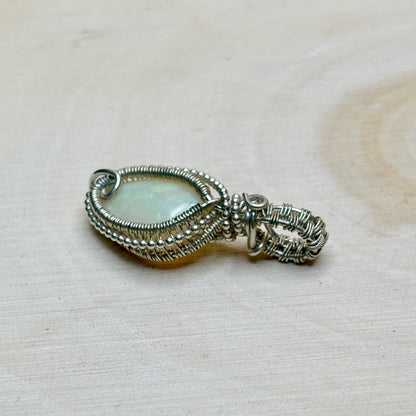 Silver wire-wrapped pendant with a central gemstone on a textured beige background