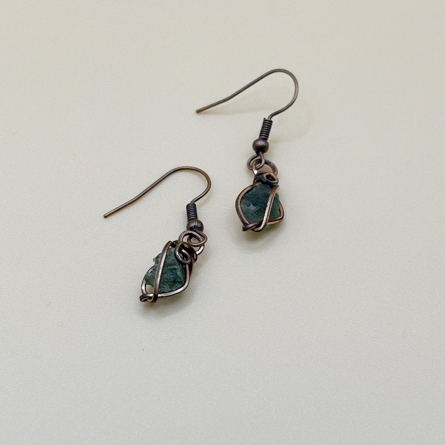 Pair of green tektite stone earrings wire wrapped in copper on a light background
