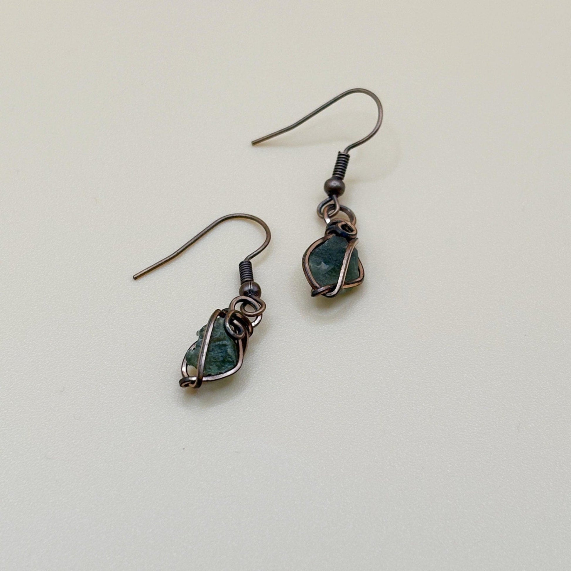 Pair of green tektite stone earrings wire wrapped in copper on a light background
