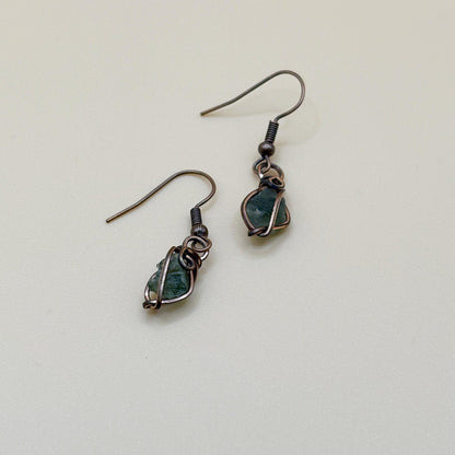 Pair of green tektite stone earrings wire wrapped in copper on a light background