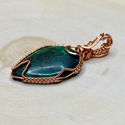 Malachite stone pendant with copper wire wrapping on a light wooden surface