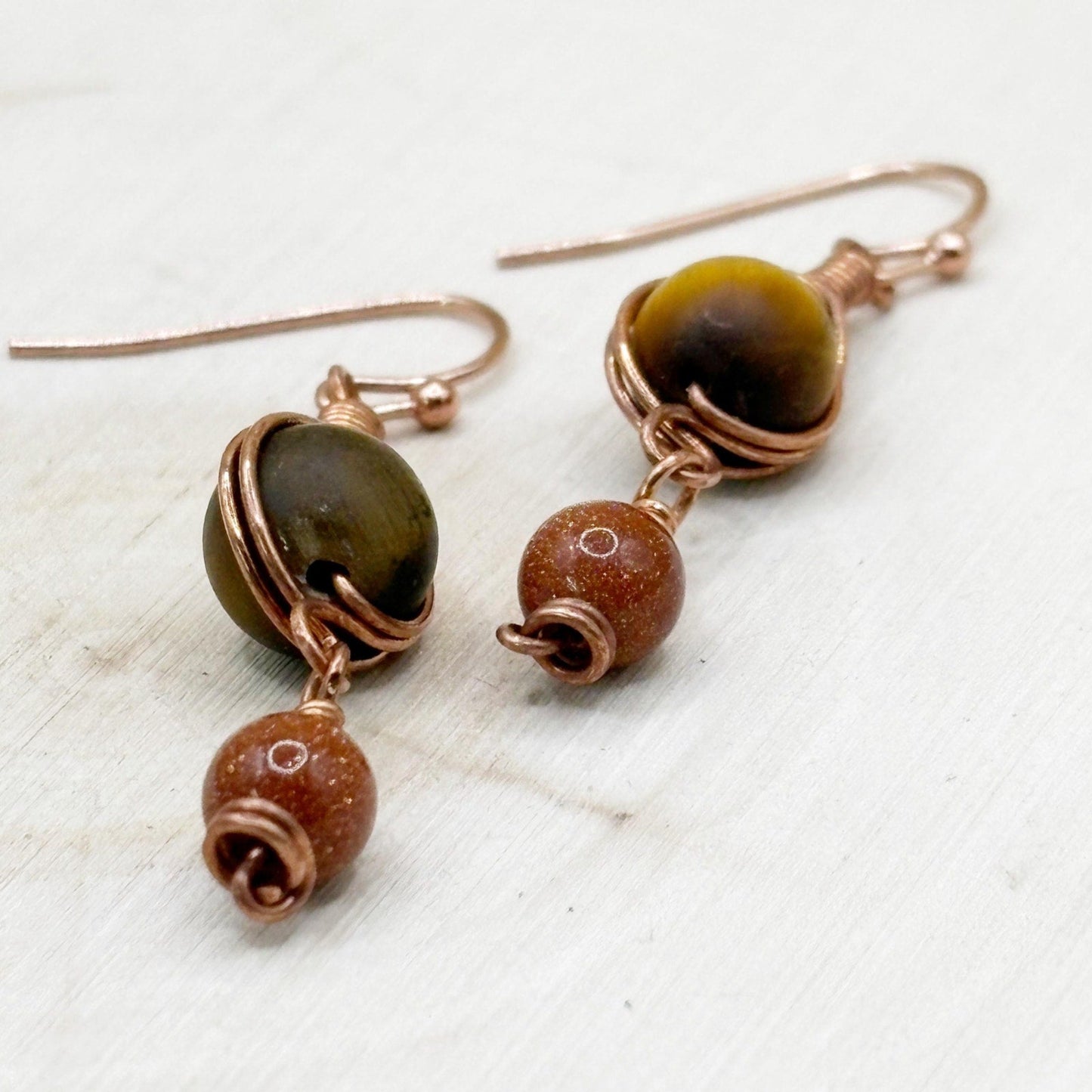 Pair of earrings with brown and gold sparkly beads on a light wooden surface