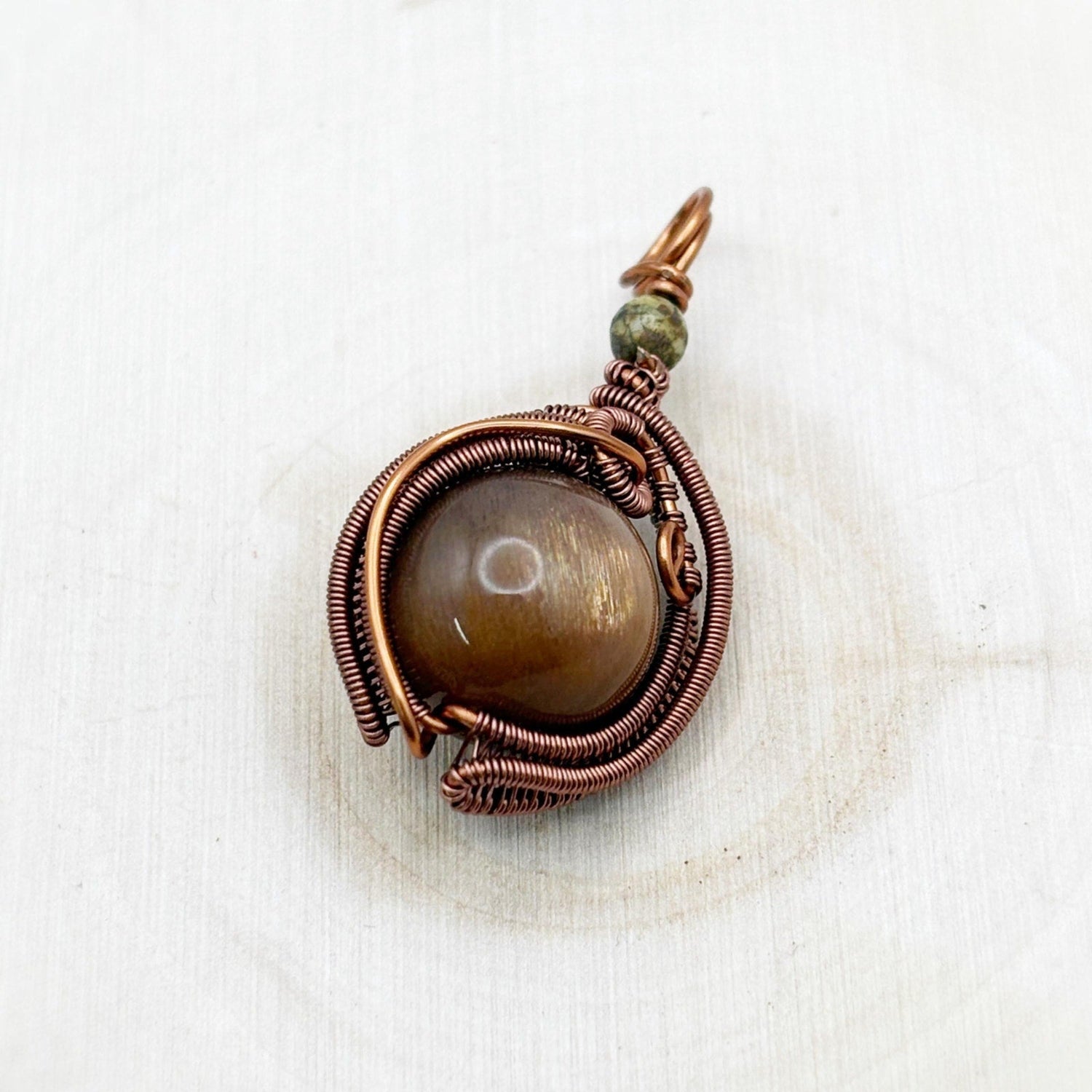 Copper-wrapped pendant with a central brown sparkly stone on a white wood background