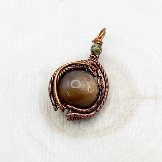 Copper-wrapped pendant with a central brown sparkly stone on a white wood background-p