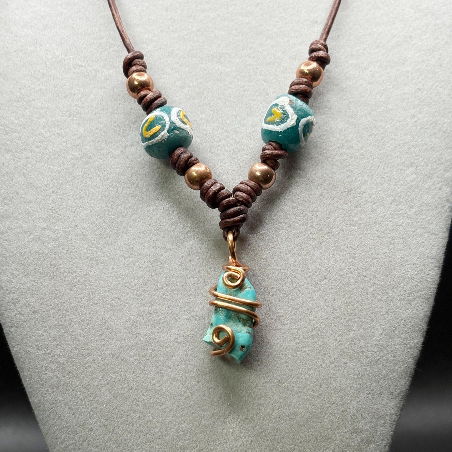 Necklace with turquoise beads and a decorative pendant on a gray surface