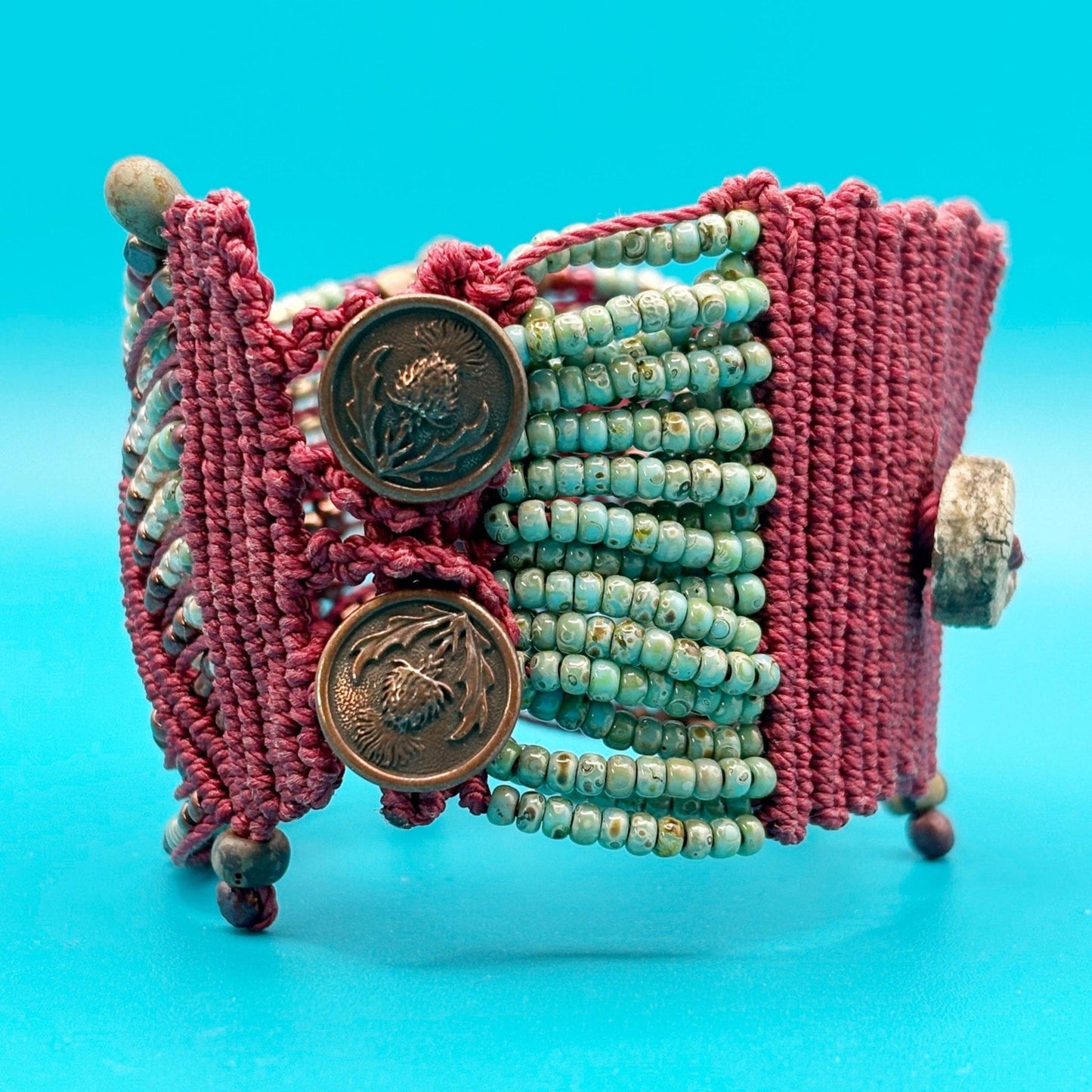 Bracelet with red woven design, turquoise beads, and copper buttons on a blue background