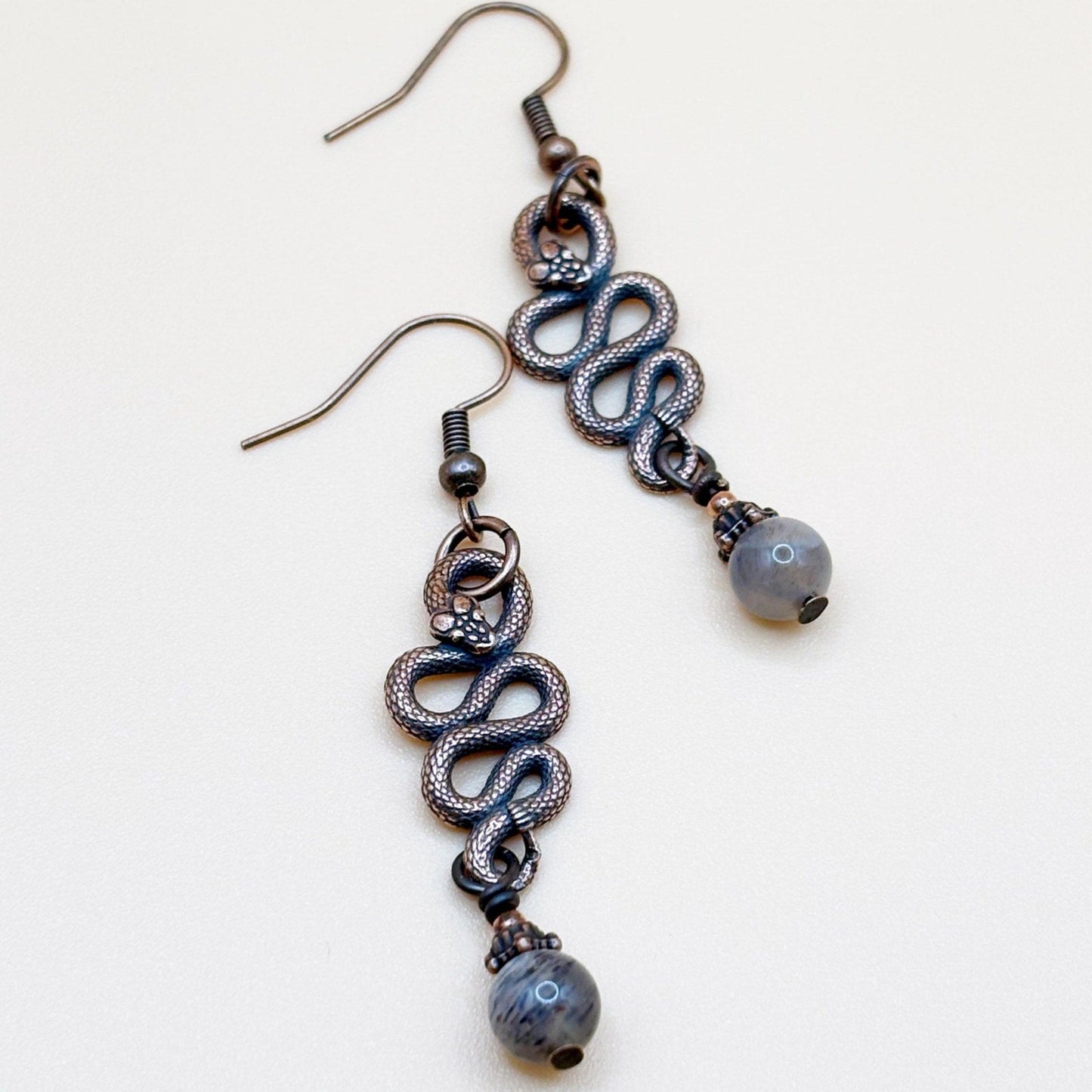 Pair of snake-shaped earrings with beads on a white background