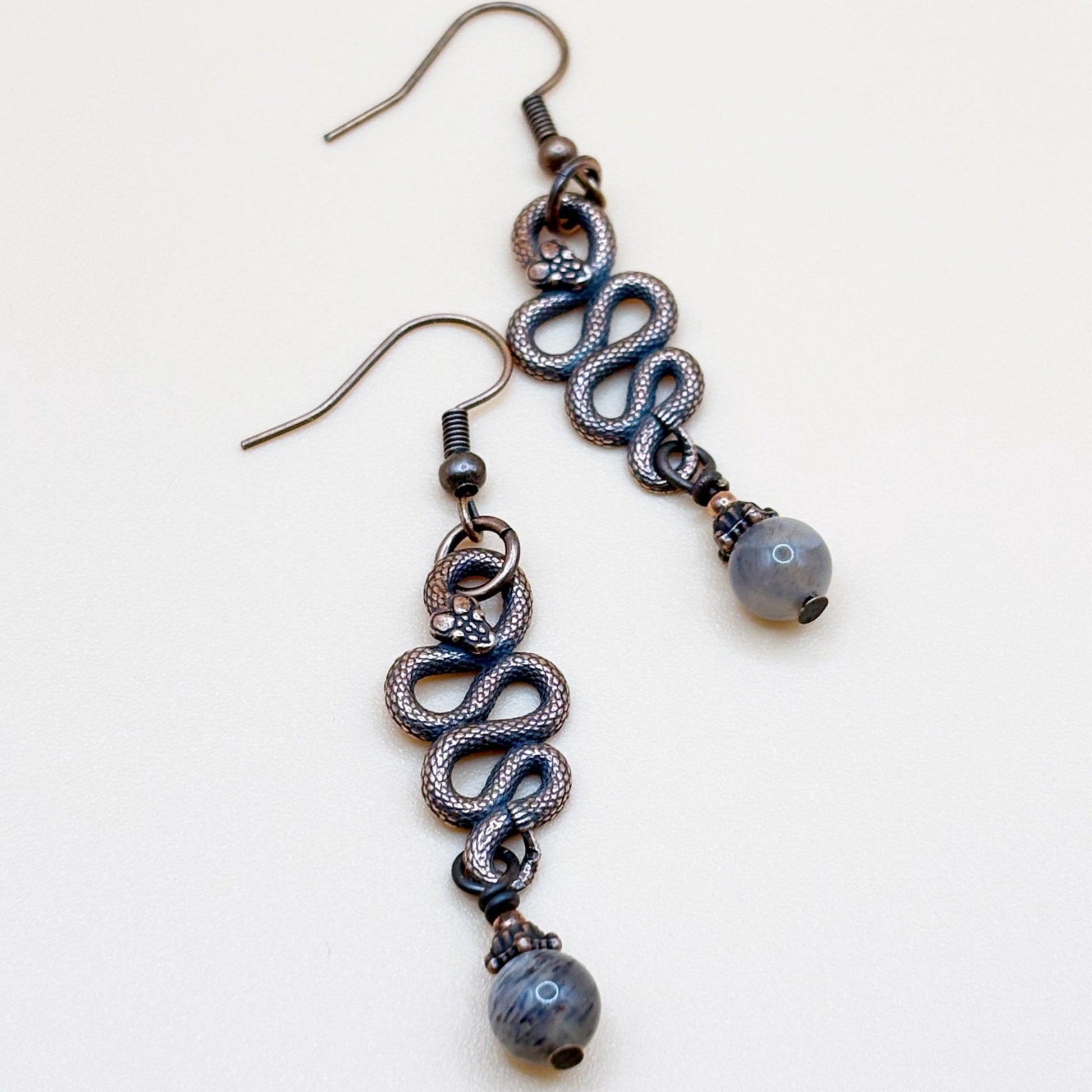 Pair of snake-shaped earrings with beads on a white background