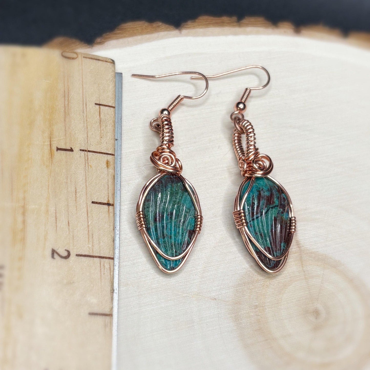 Pair of earrings with green stone and copper wire wrapping on a wooden surface.