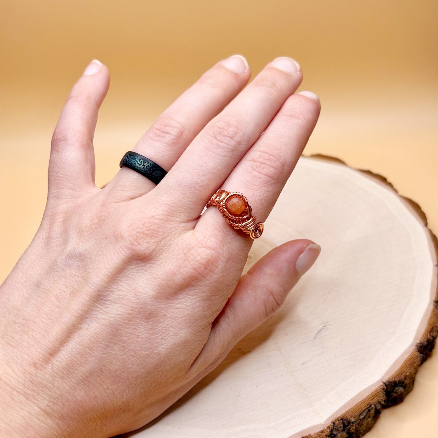 Hand wearing two rings on a wooden surface with a warm background