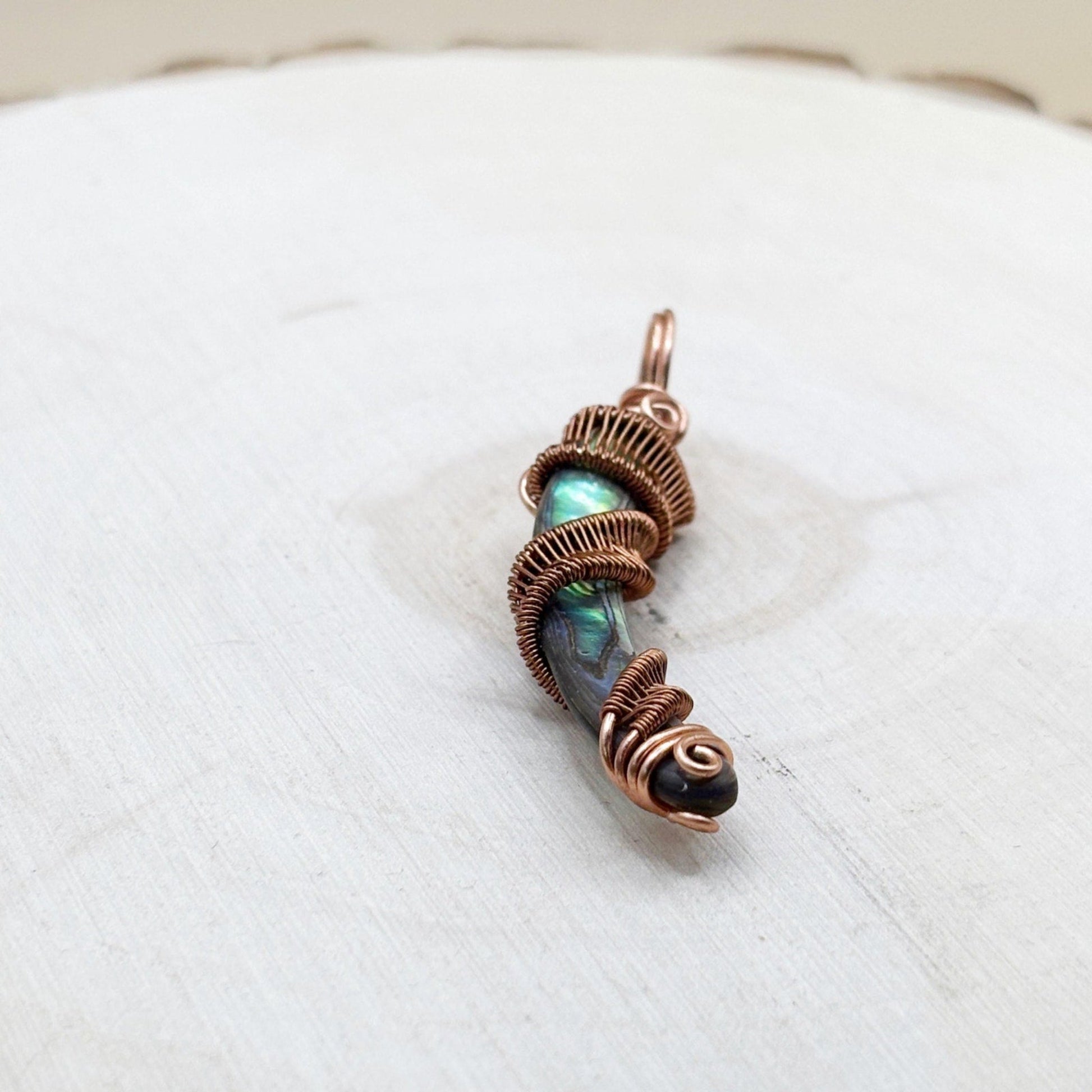 Copper-wrapped pendant with a central shell on a white background