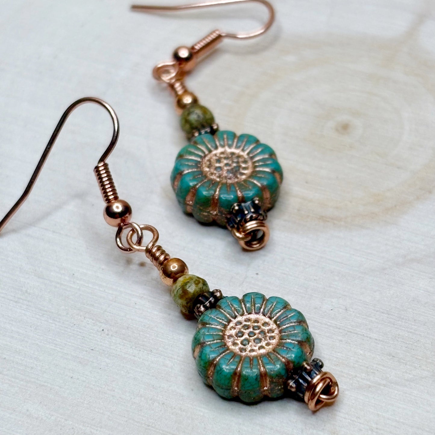Pair of earrings with turquoise and copper floral designs on a light background