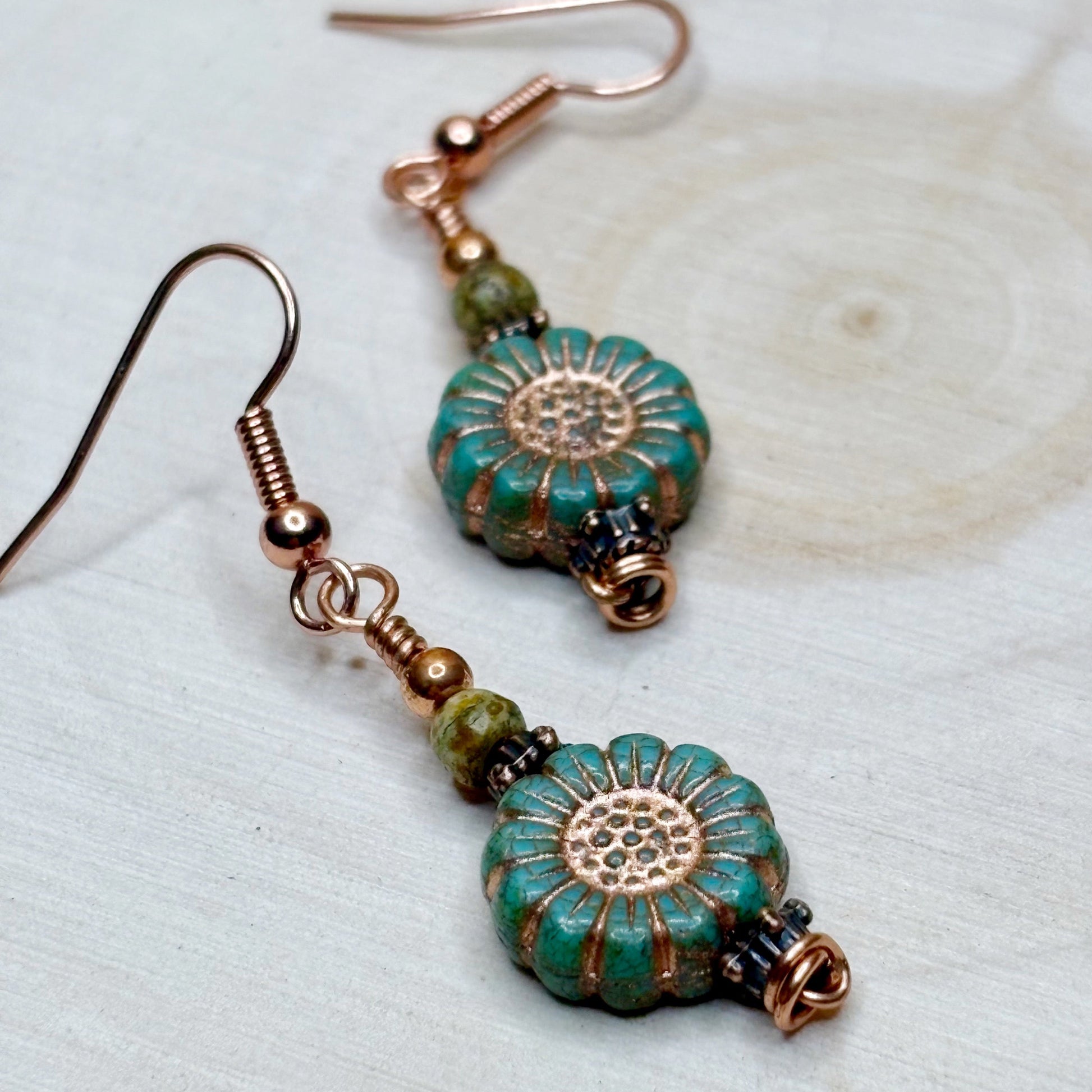 Pair of earrings with turquoise and copper floral designs on a light background