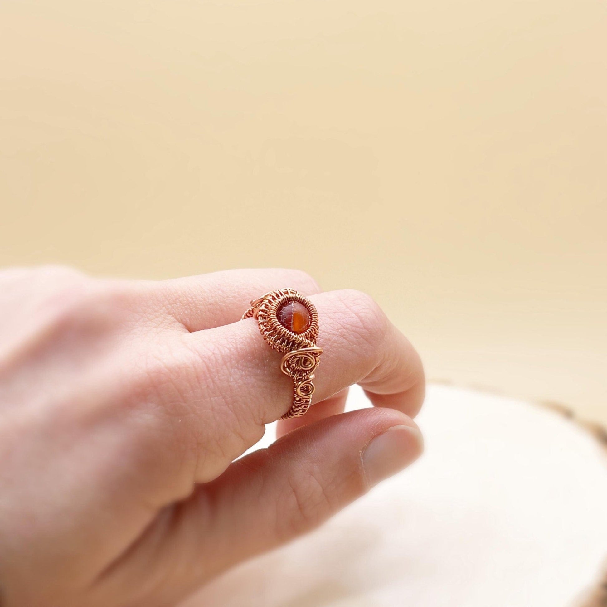 Hand wearing a copper wire-wrapped ring with a red gemstone on a blurred background