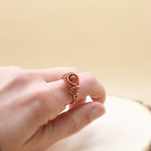 Hand wearing a copper wire-wrapped ring with a red gemstone on a blurred background