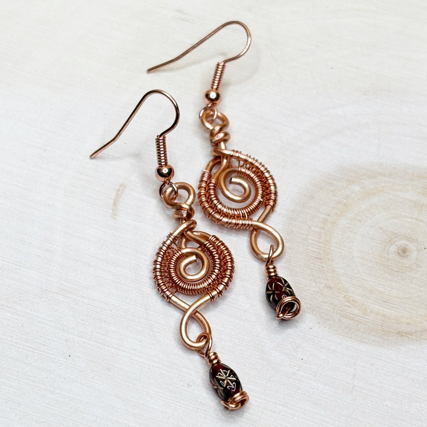 Copper wire-wrapped earrings with beads on a light background