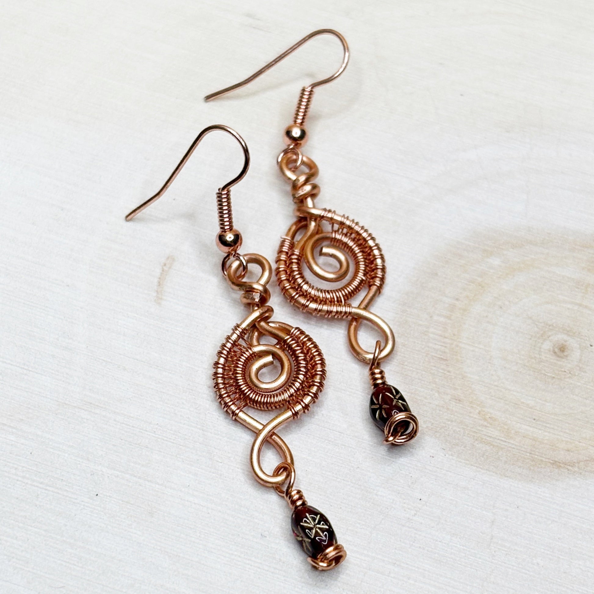 Copper wire-wrapped earrings with beads on a light background