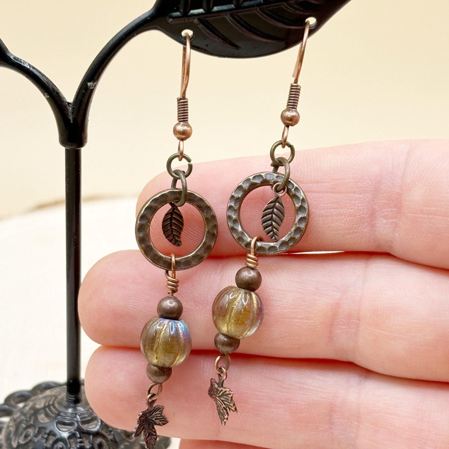 Pair of copper and glass beaded earrings held in a hand against a neutral background