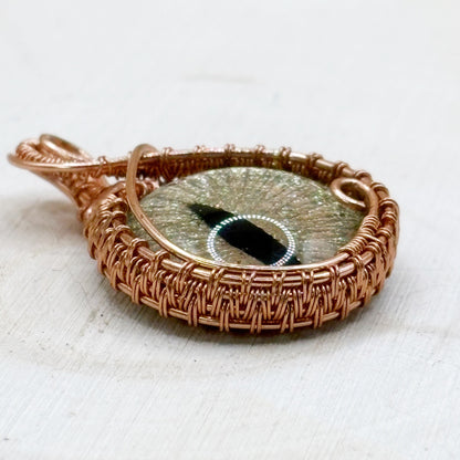 Copper-wrapped pendant with a central glass dragon eye on a white wood background