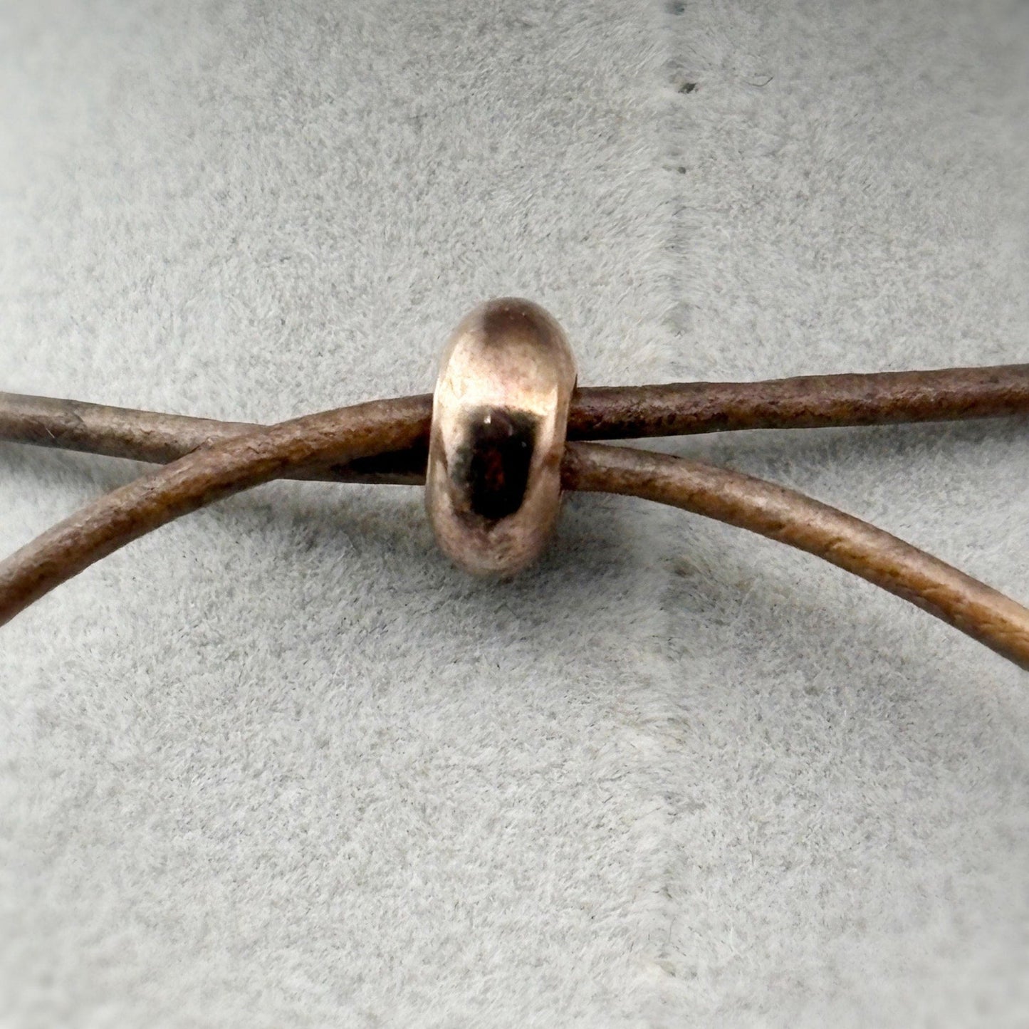 Copper bead on a leather cord against a gray background