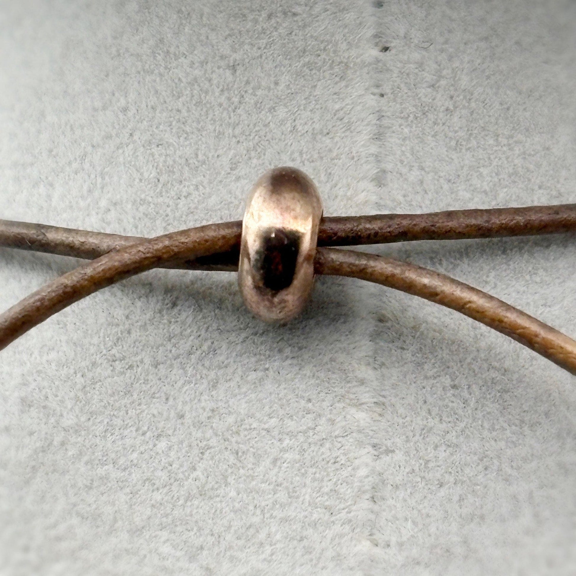 Copper bead on a leather cord against a gray background