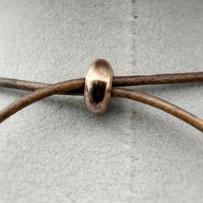 Copper bead on a leather cord against a gray background