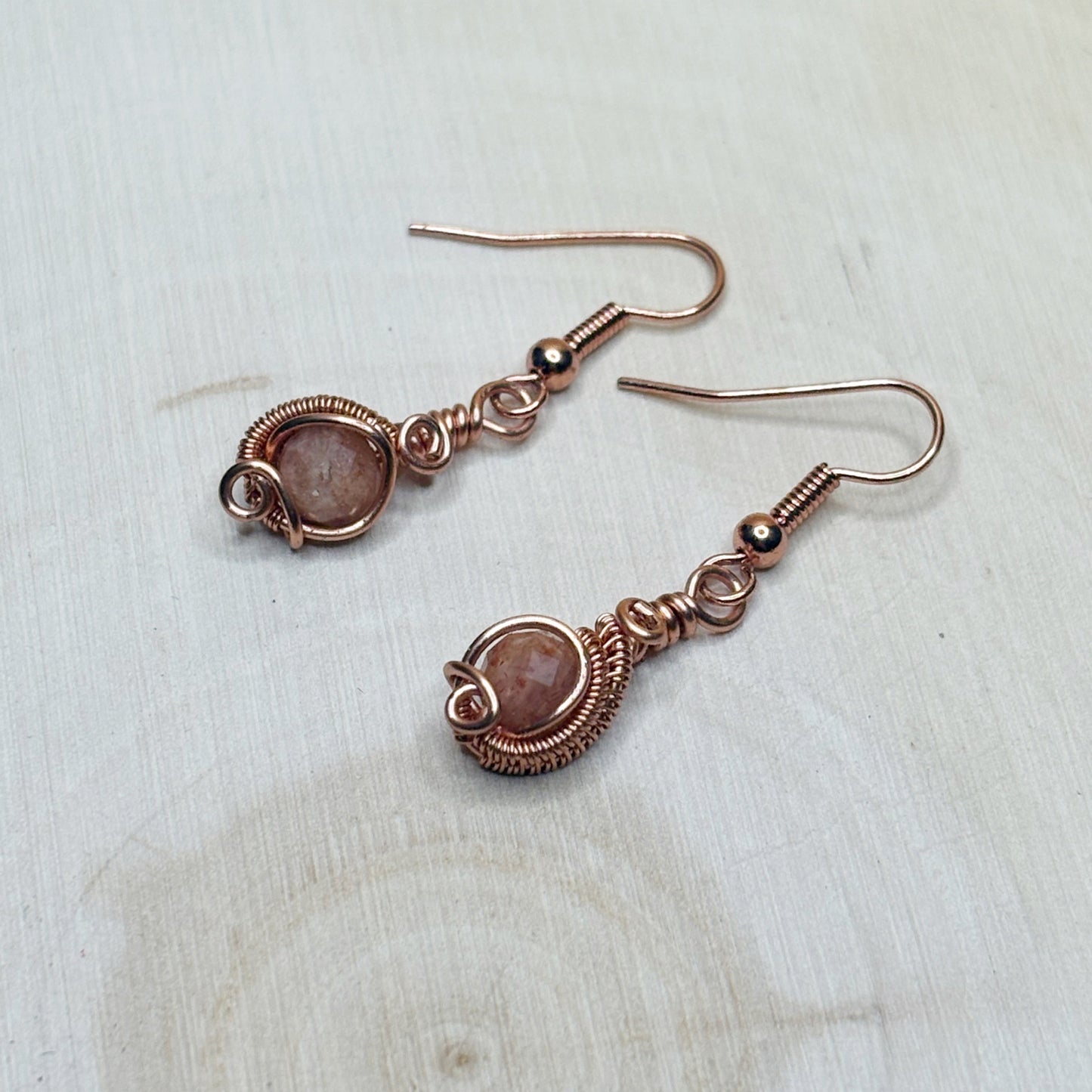 Pair of copper wire-wrapped earrings with gemstones on a light wooden surface