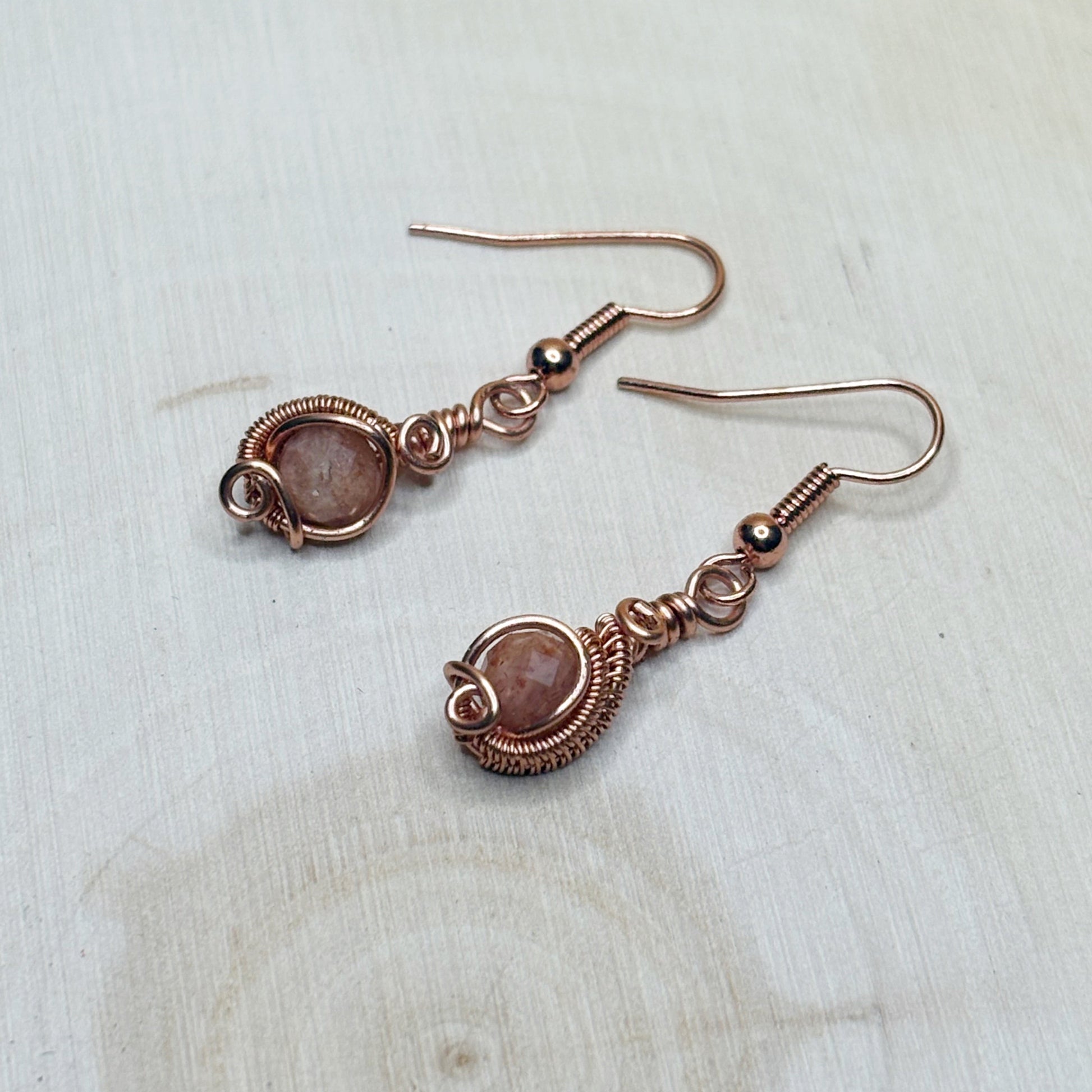 Pair of copper wire-wrapped earrings with gemstones on a light wooden surface