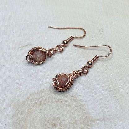 Pair of copper wire-wrapped earrings with gemstones on a light wooden surface